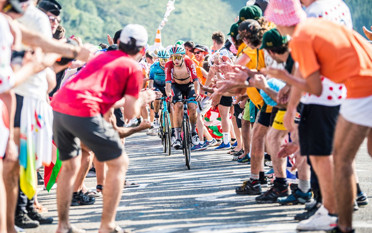 A cyclist with his jersey hanging open rides through a crowd of fans on a mountain stage of the Tour de France.