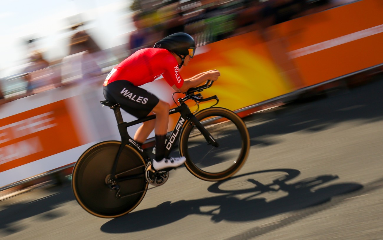 Welsh time-trialist in a red jersey during a race on a black time-trial bike with a disc wheel.