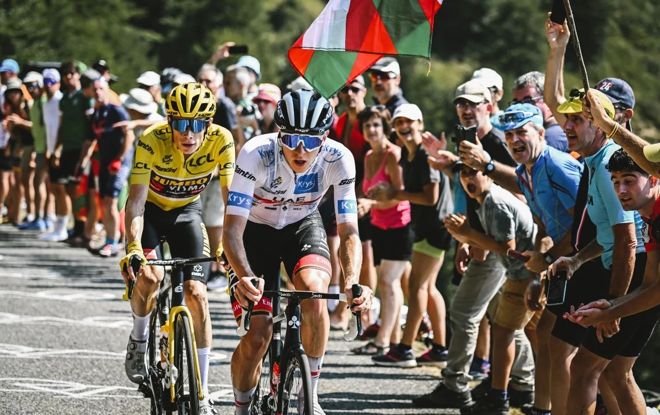 Jonas Vingegaard and Tadej Pogacar pedal past cheering spectators at the Tour de France.