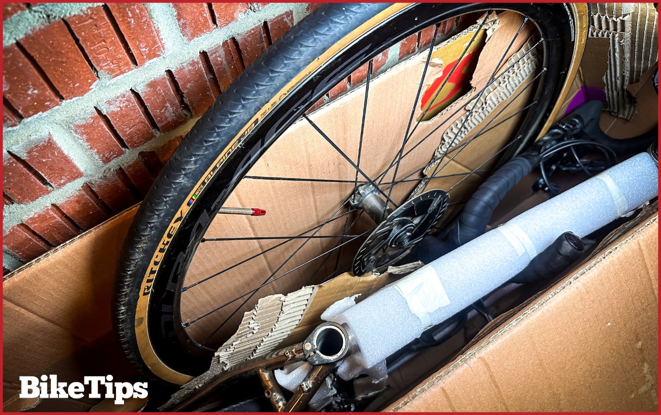 A bike wheel going into a bike shipping box.