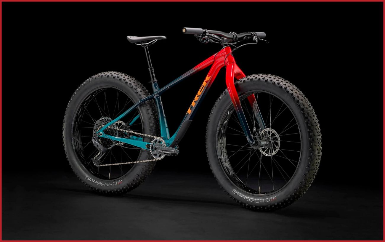 Red, black and turquoise Trek Farley mountain bike with fat tyres with a black background.