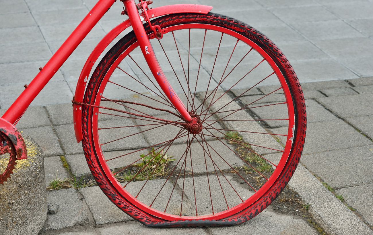 A red and black bike rests upon the pavement with a flat front tire. 