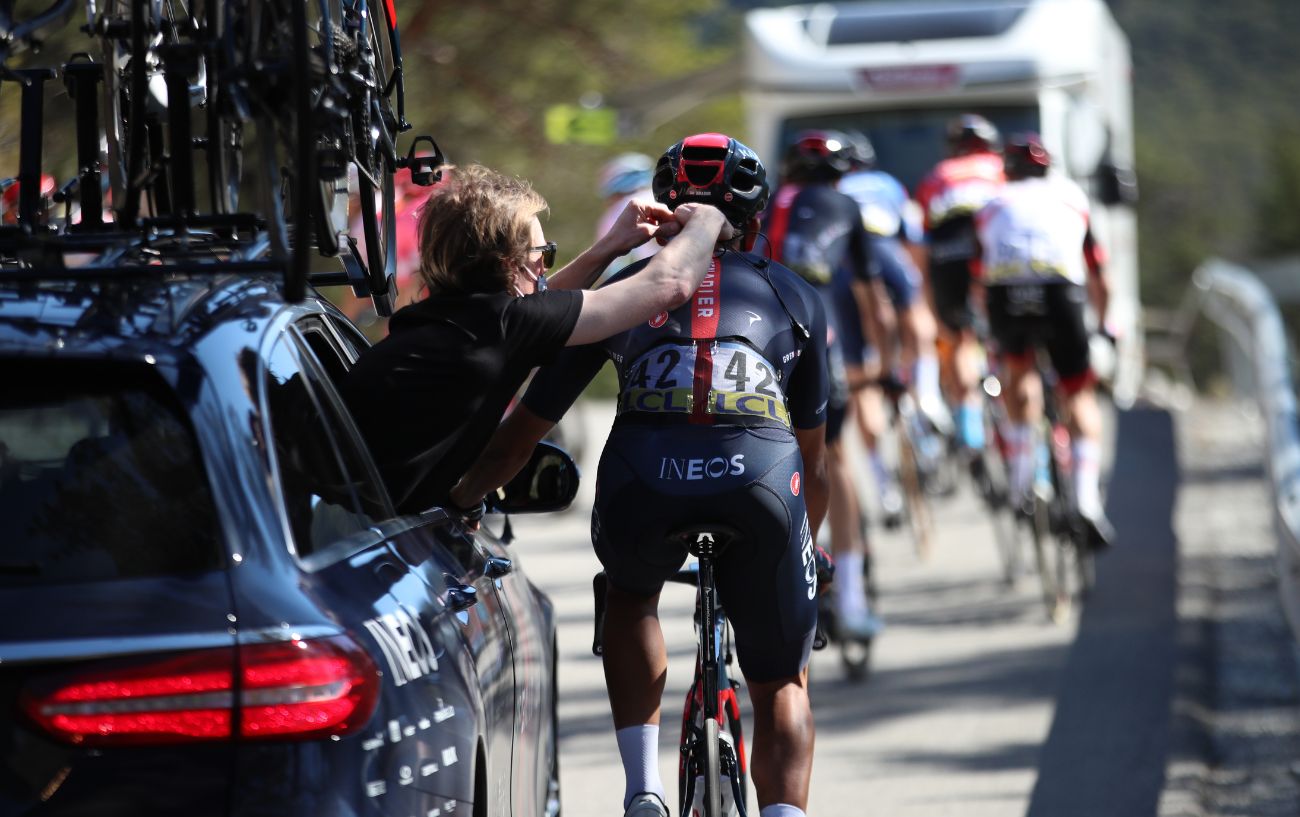 A Tour de France mechanic makes repairs to a rider's helmet from the team car while the cyclist continues riding.