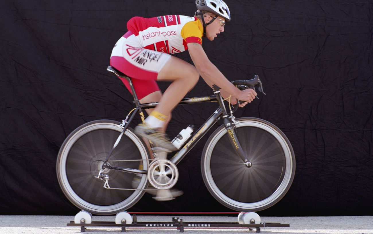 A cyclist wearing red and white cycles on and indoor roller.