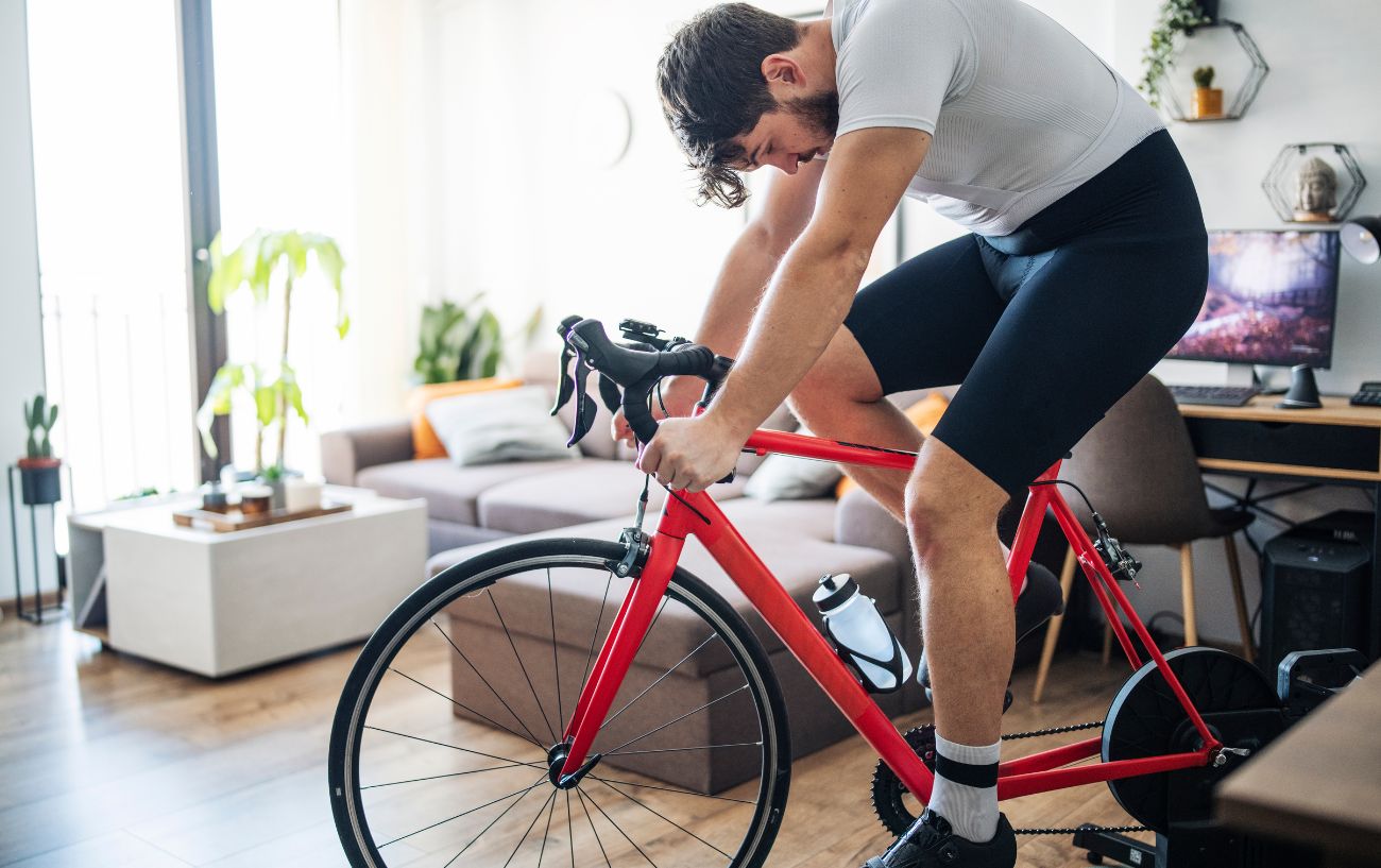 Man wearing white and black sits on a red indoor trainer in a well-lit room. 