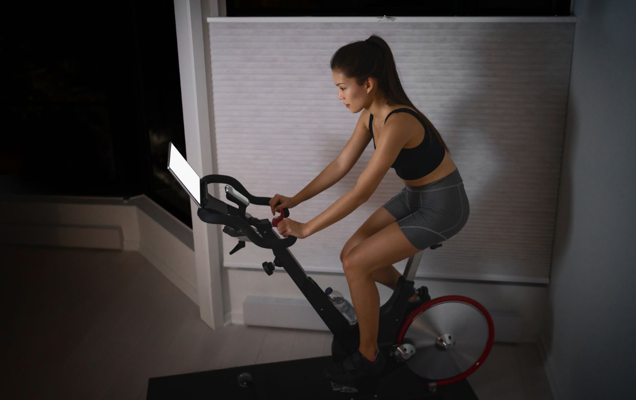 Woman wearing black and grey cycles on an indoor bicycle with the lights off. 