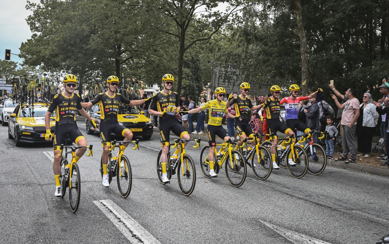 Team Jumbo-Visma ride with their arms around each other to celebrate winning the Tour de France 2023.