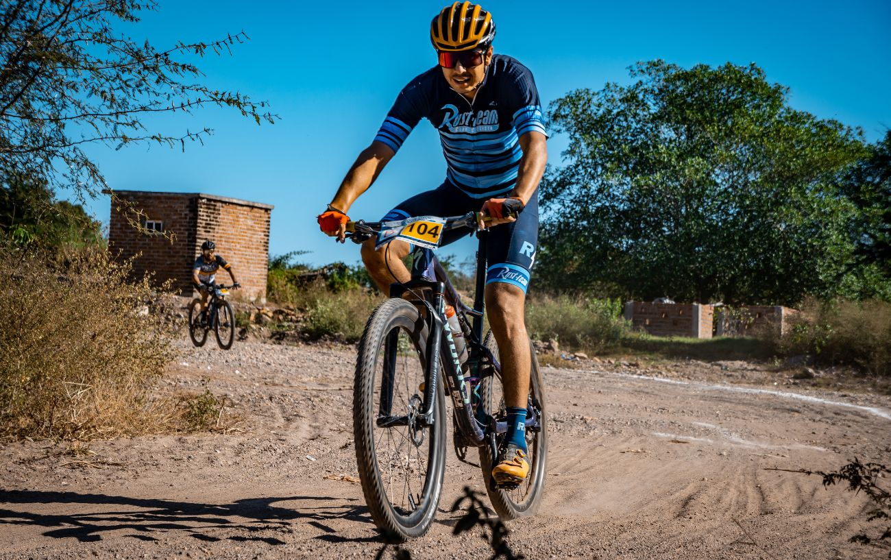 Mountain biker wearing an orange helmet and blue bib shorts cycle on a specialized mountain bike.