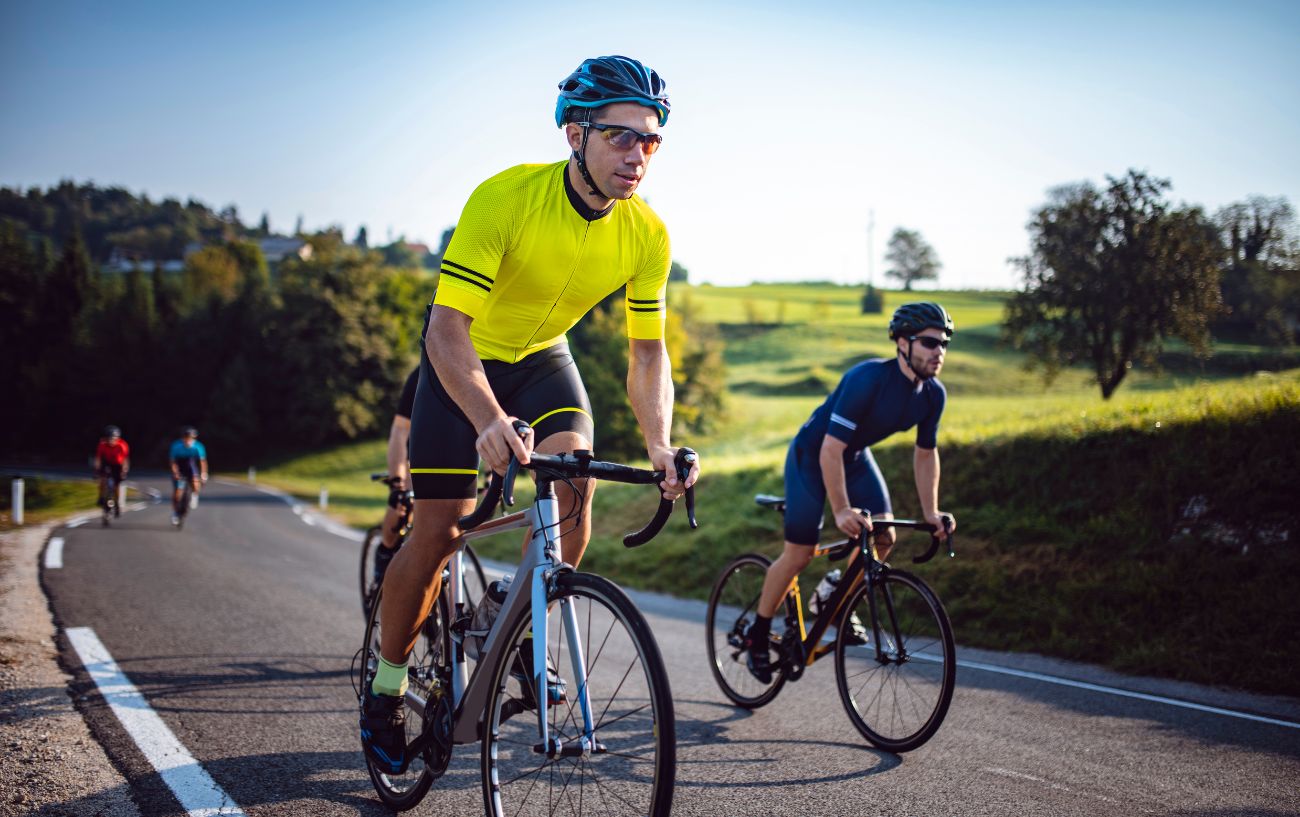 Three cyclists cycle uphill wearing a yellow top and standing out of the saddle. 