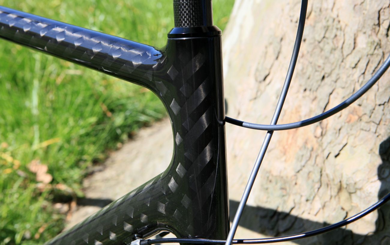 Carbon road bike frame next to a wall with grass in the background. 
