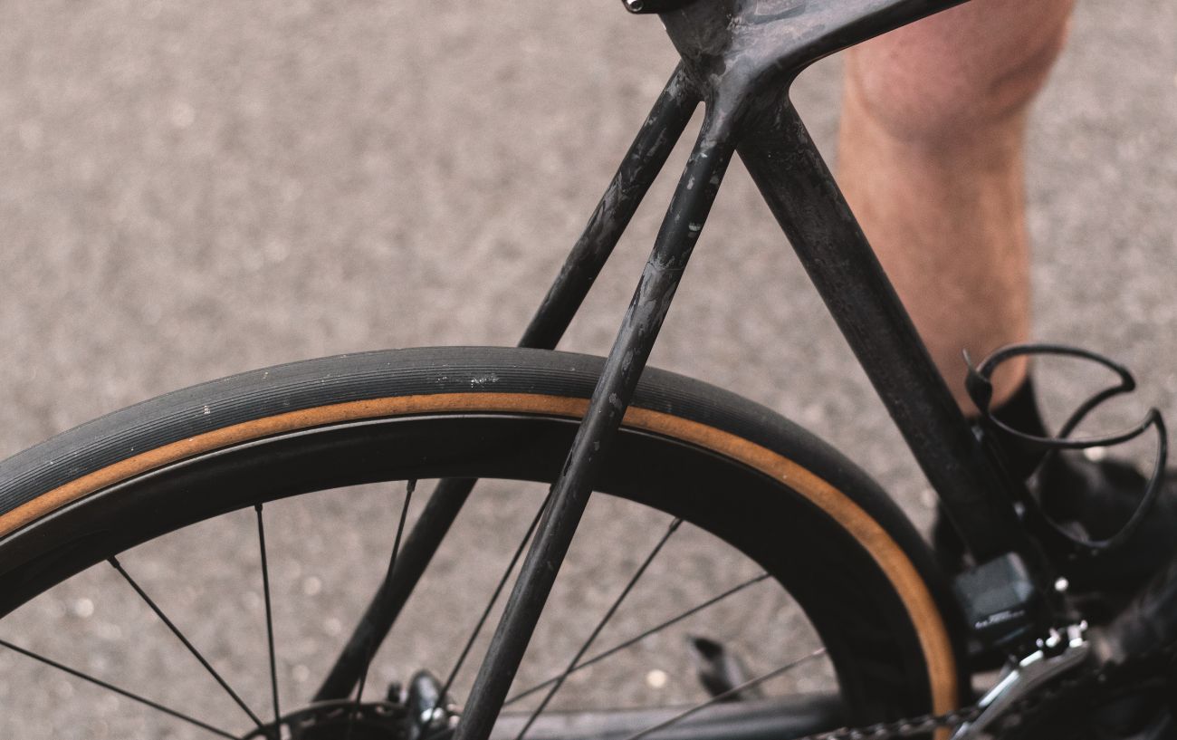 A black and tan back wheel of a carbon framed road bike. 