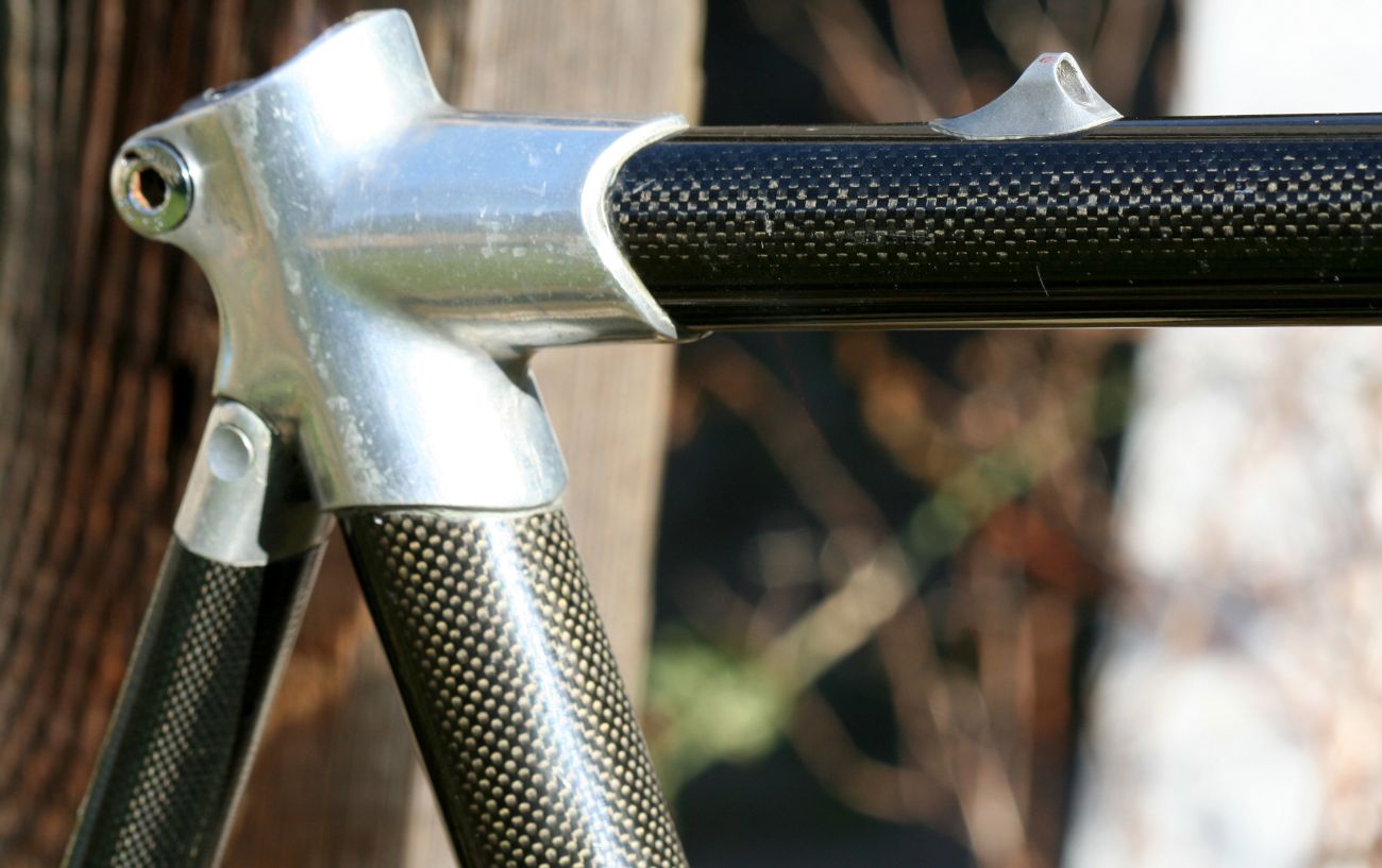 Three points of a carbon road bike frame intersect with a blurred out background. 