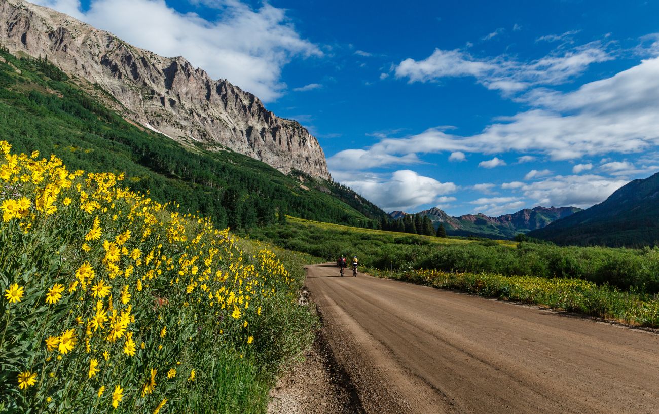 Two cyclists ride a gravel path beneath a cliff while biking across America.