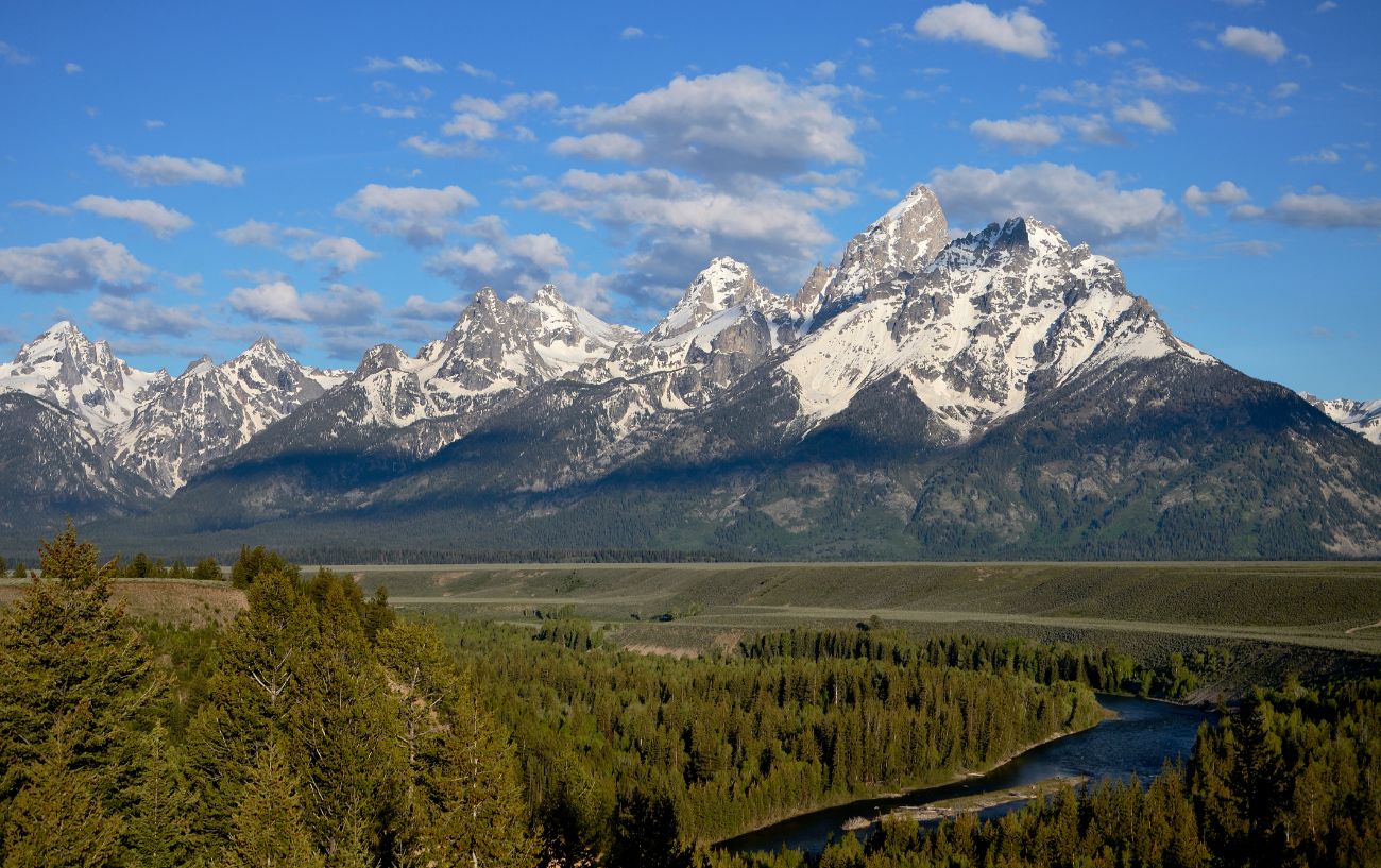View of a river and grassy plain in front of a mountain range in Wyoming.