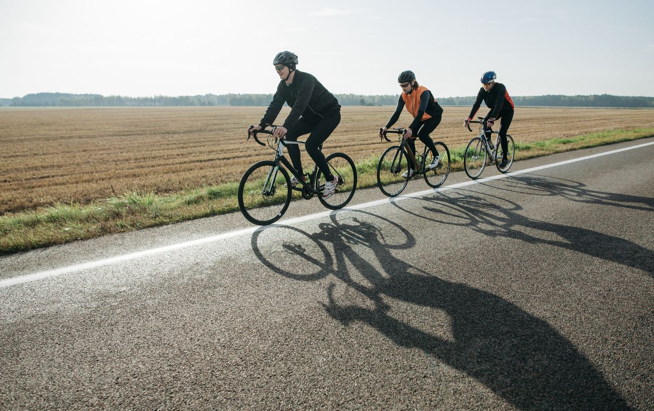 Three cyclists ride past a field at sunrise.