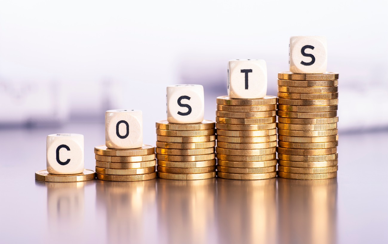 A pile of pound coins rests on a surface with the word costs on top.