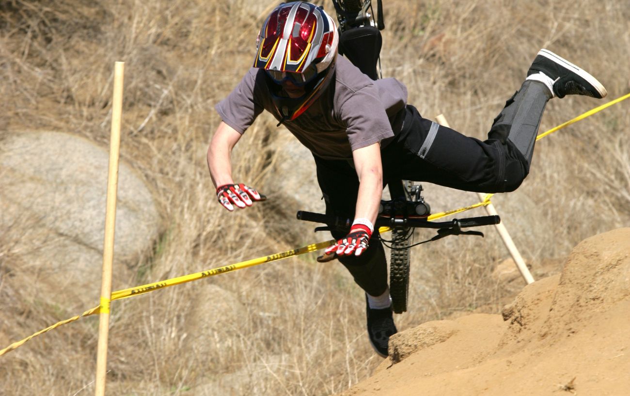 A mountain biker wearing a full face helmet crashes on a downhill course.