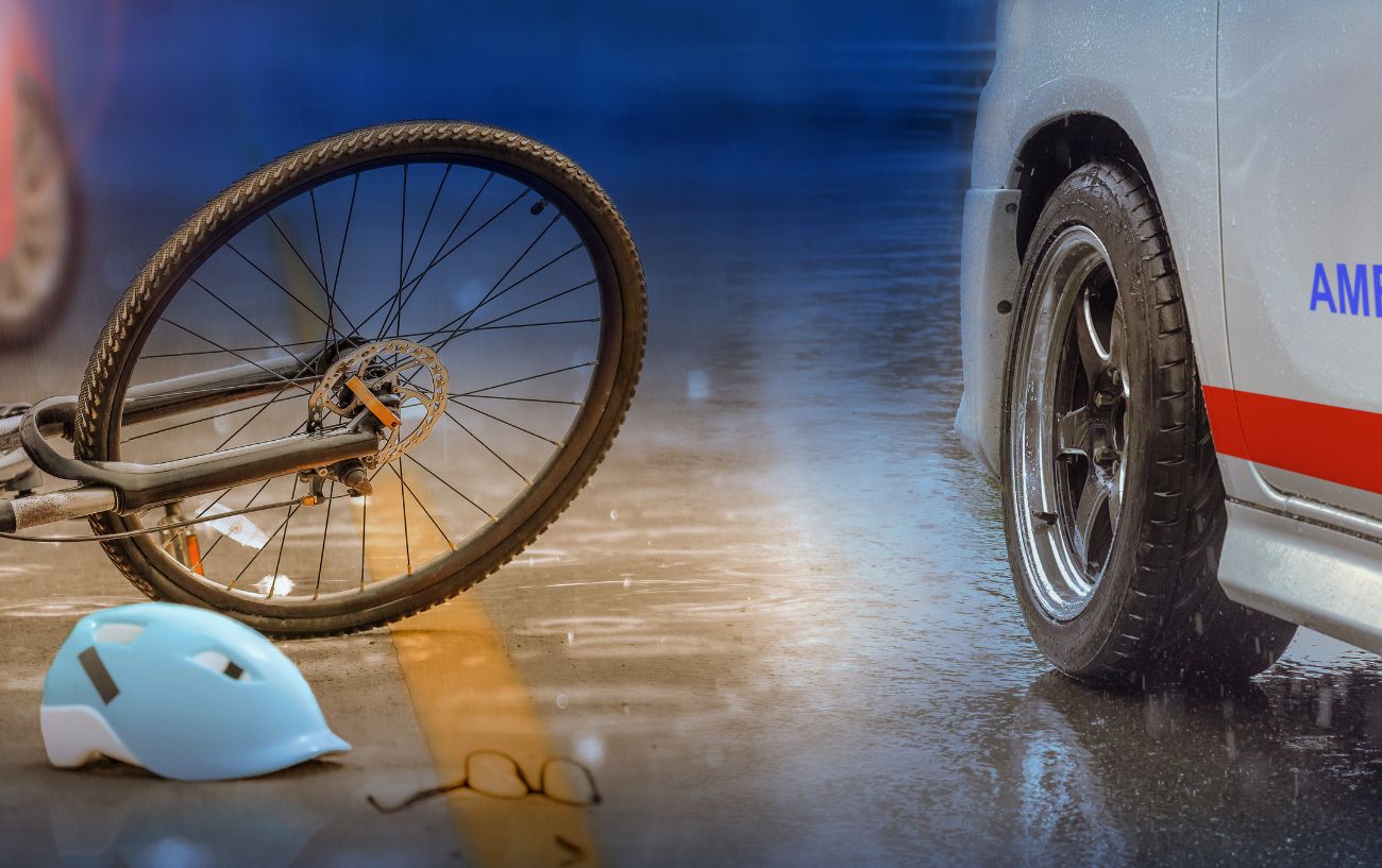 A bicycle and a bike helmet lie on the ground next to an ambulance.