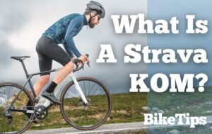 Man wearing blue top and black shorts cycles uphill with the words "What Is A Strava KOM?" in the foreground.
