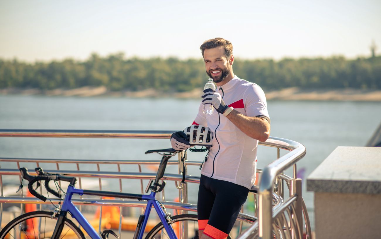 A cyclist laughs as he pauses for a drink on his blue road bike.