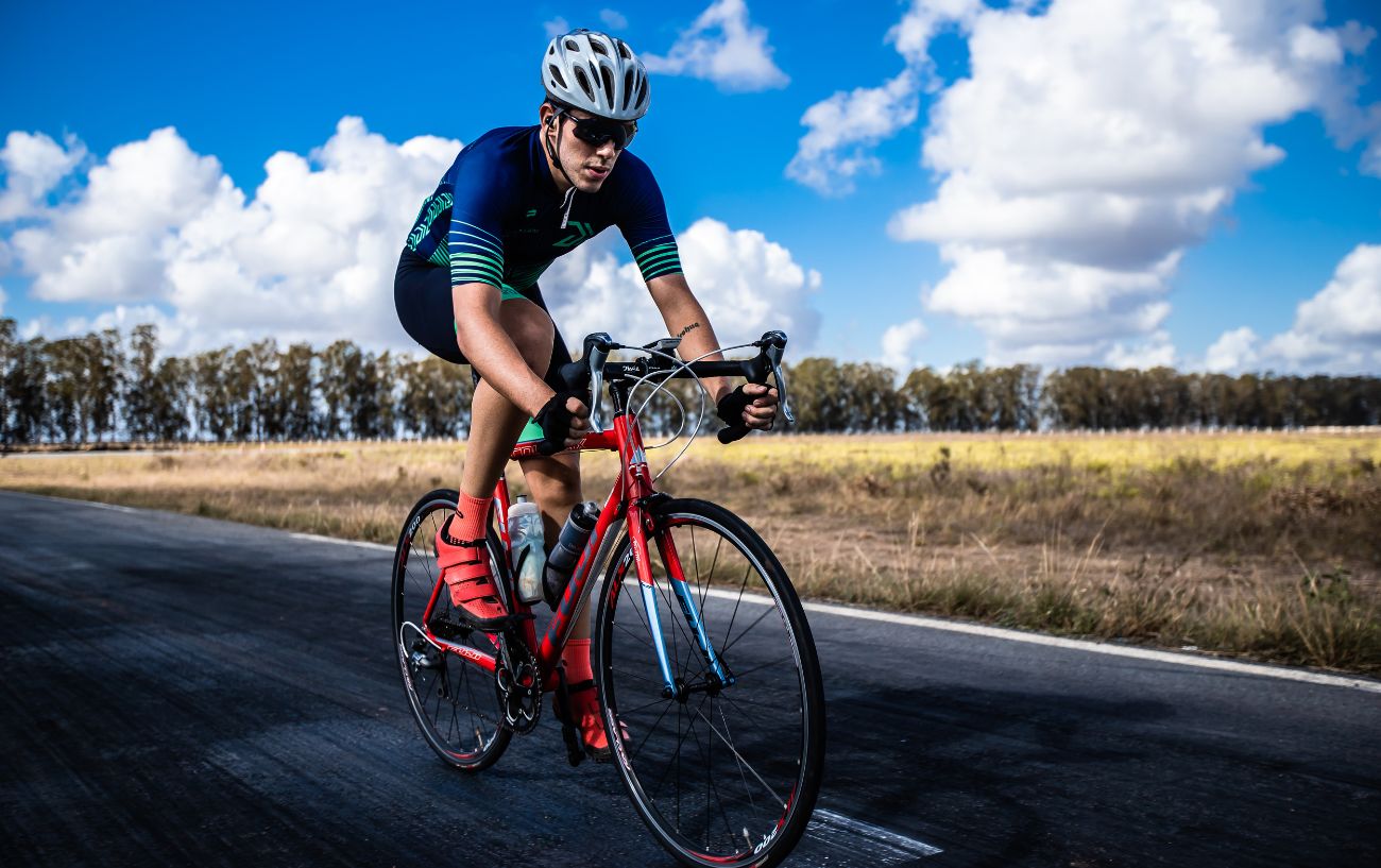 A cyclist in full lycra riding a red road bike on a sunny day.