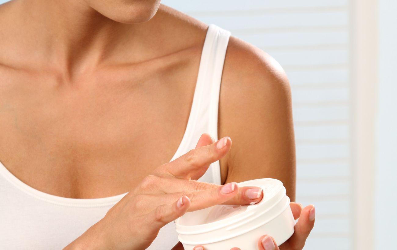 A woman wearing a white top has hands in a tub of cream.