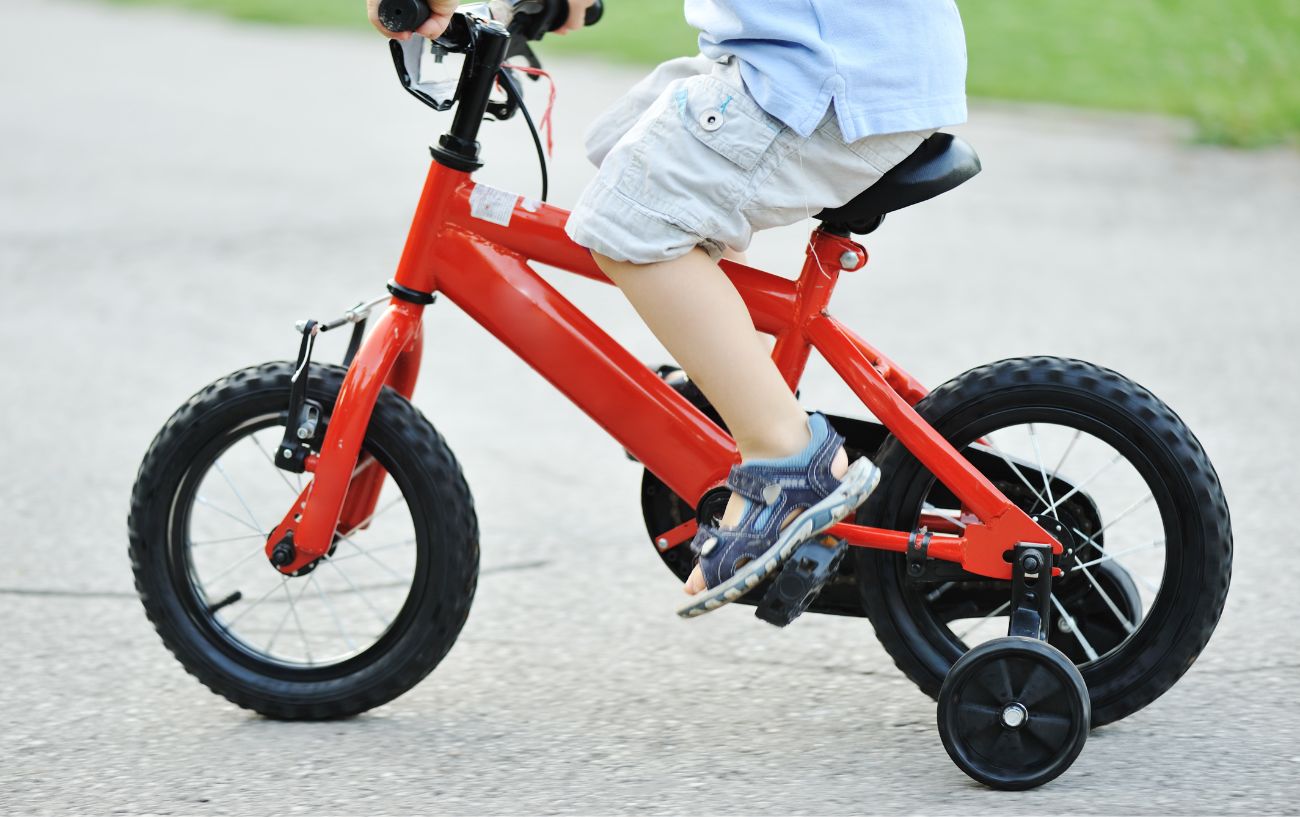A child rides a red bike with training wheels.