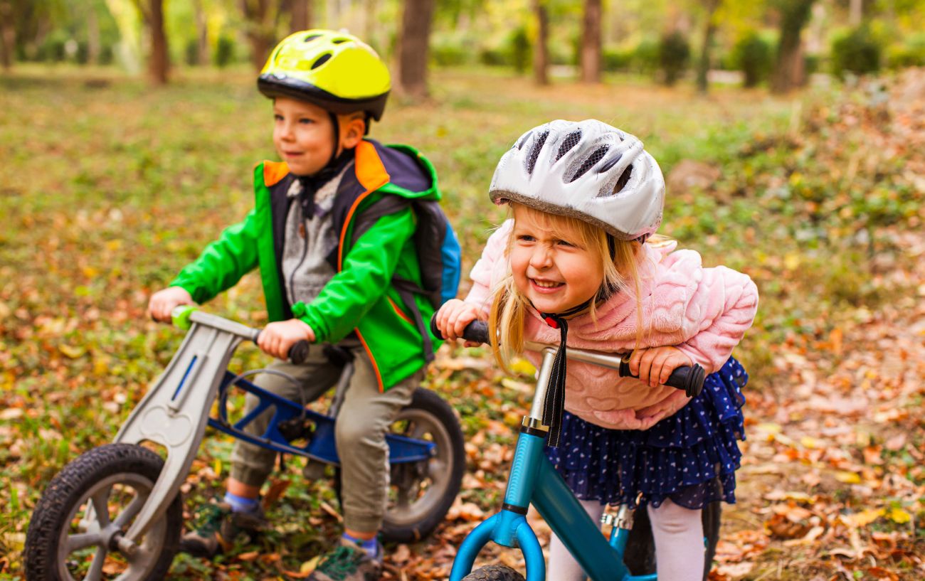 Two kids with helmets on stop on their balance bikes in a forest.