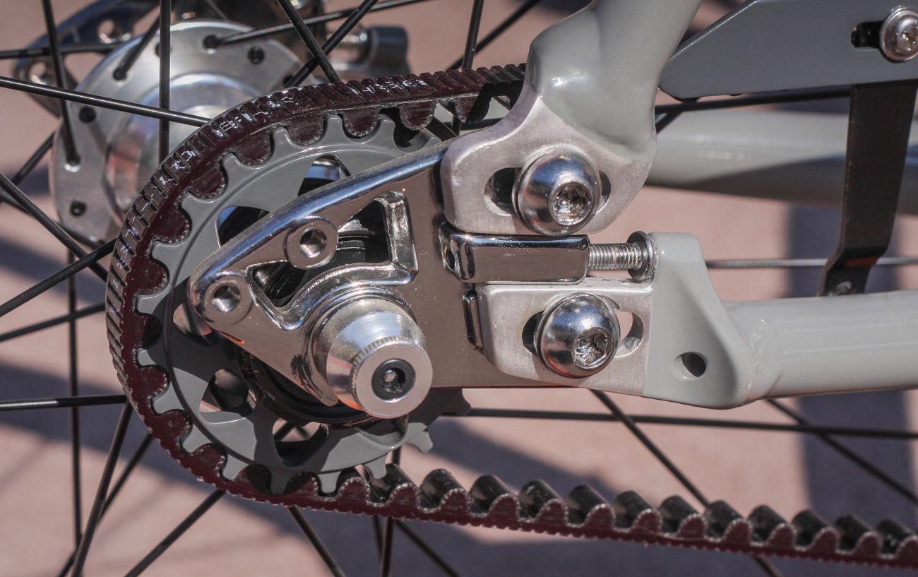 A close up of the belt drive on a grey bicycle.