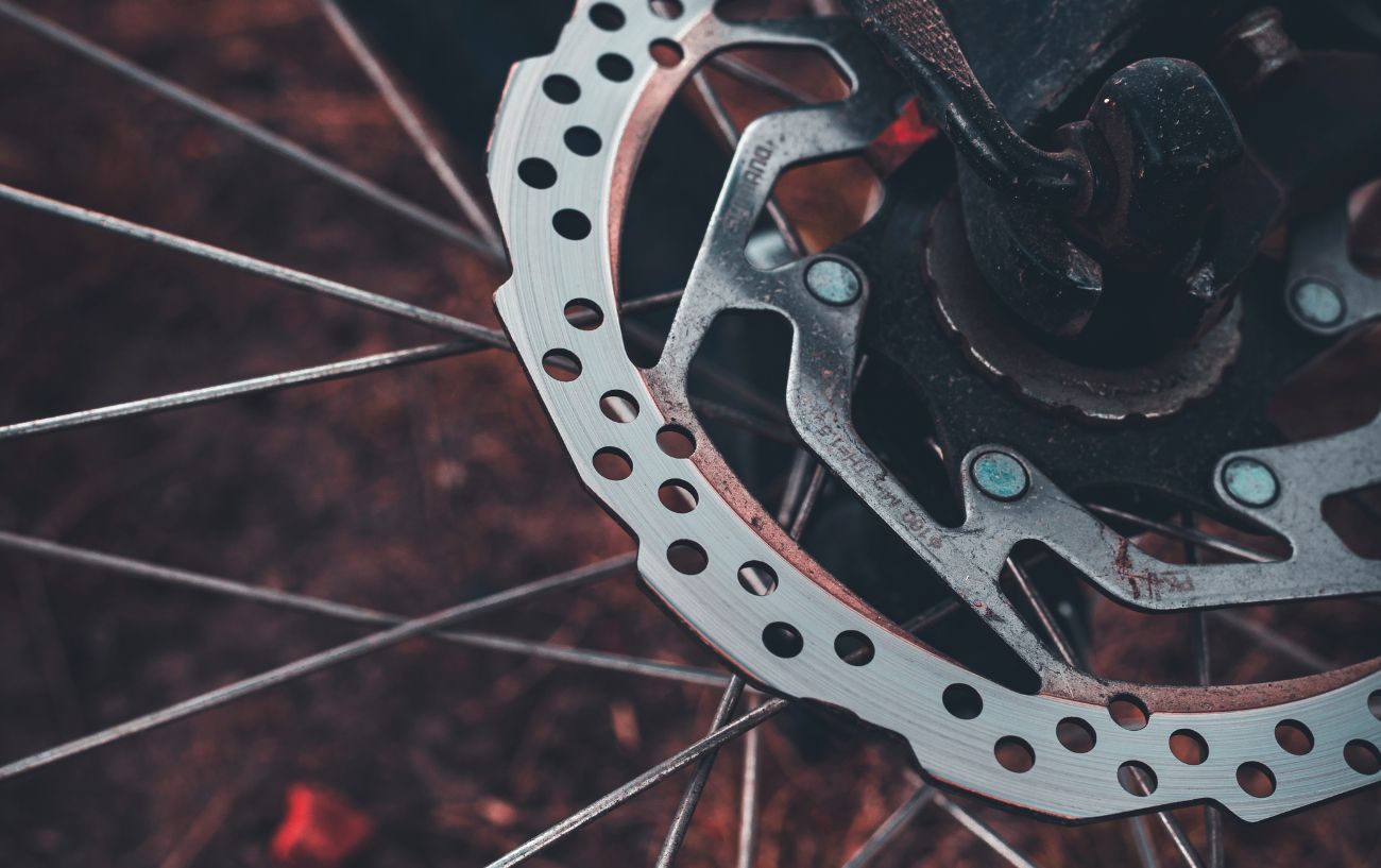 A well used disc brake with wheel spokes behind it.