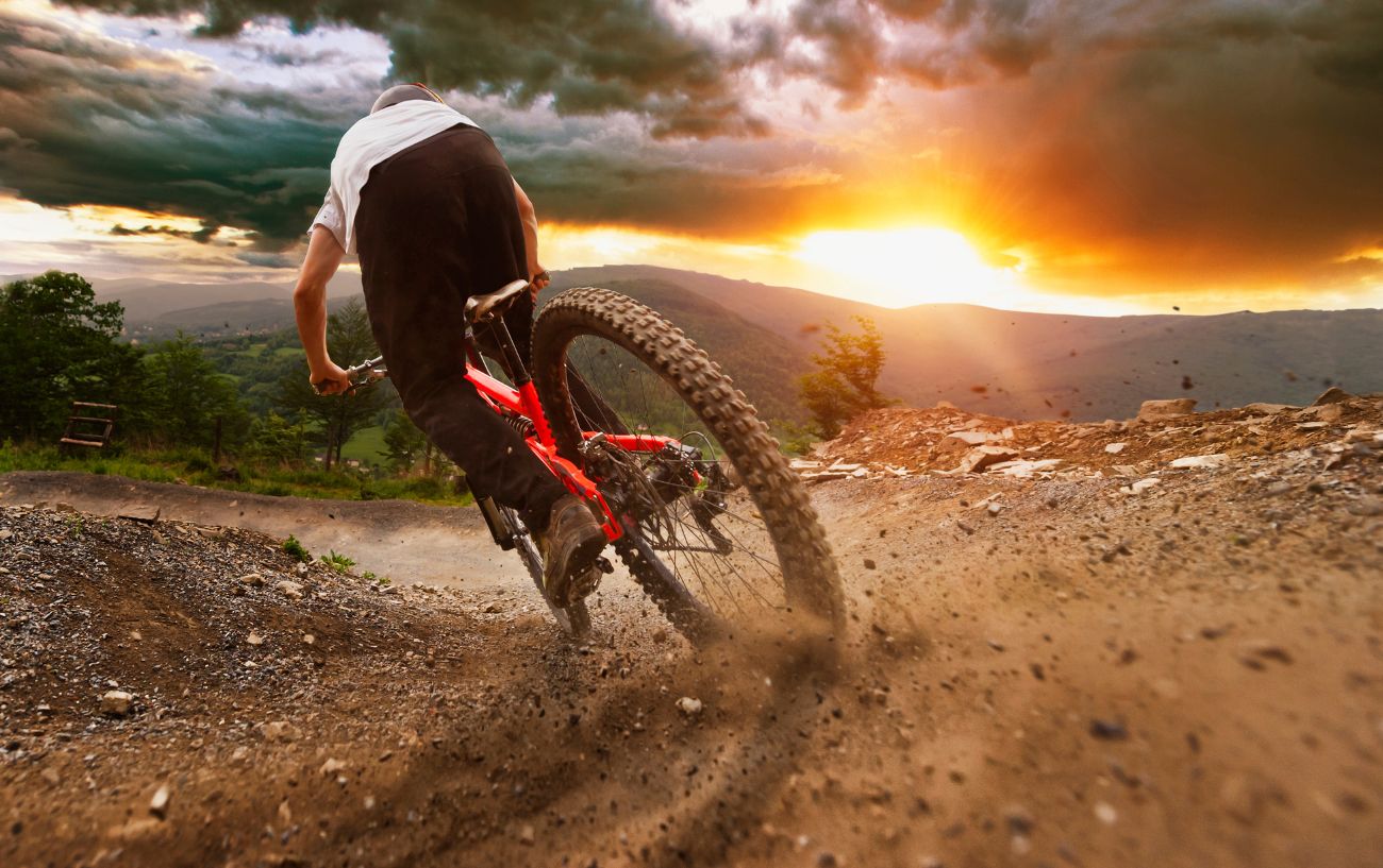 A mountain biker skids down a trail with a sunset in the background.