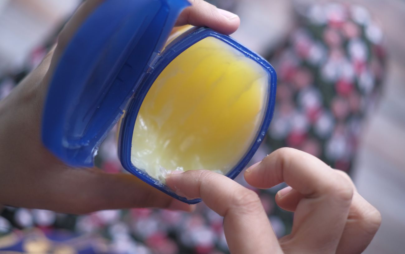 Someone dips their finger into a blue tub of Vaseline.