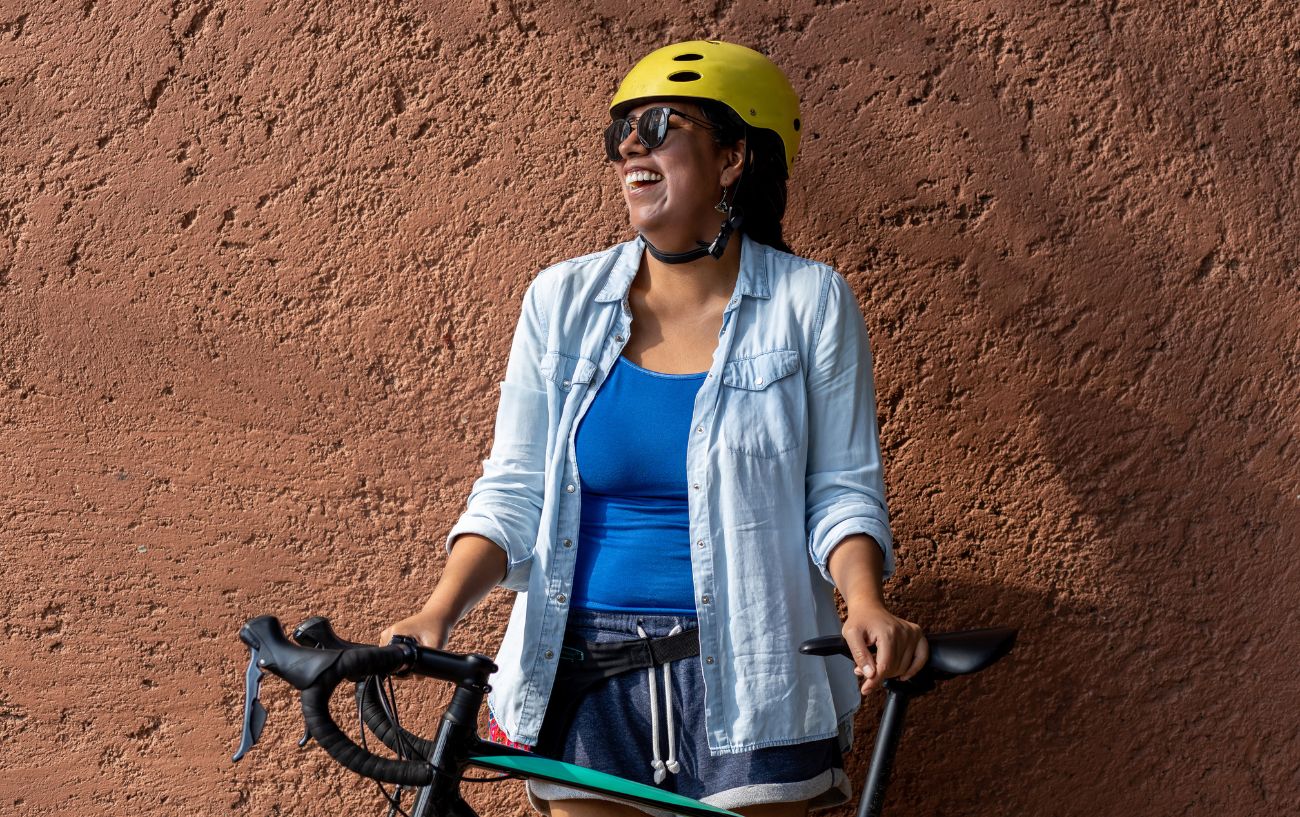 A woman pushing a black road bike laughs at a bicycle joke.