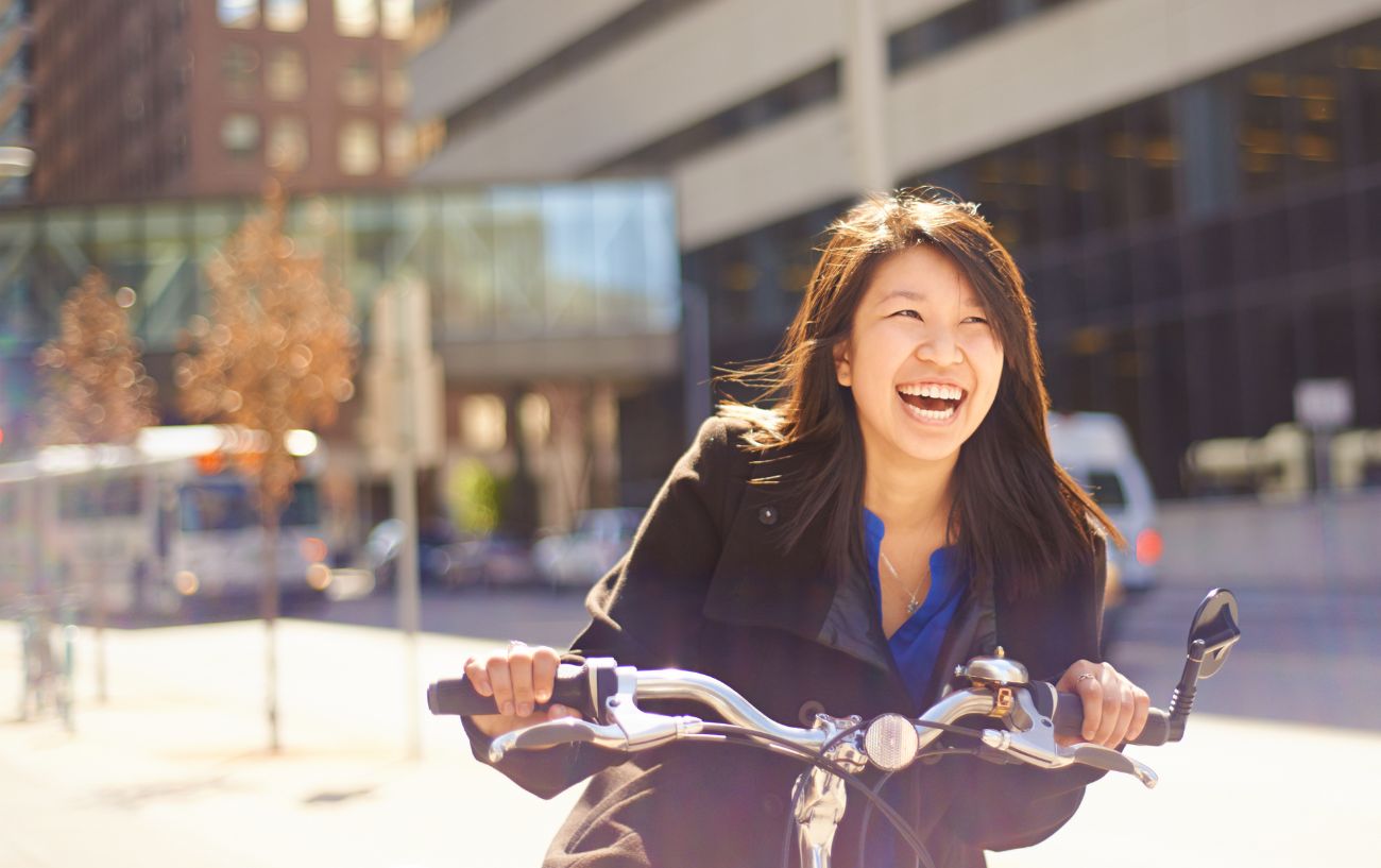 A woman in a black coat laughs while riding a bike.
