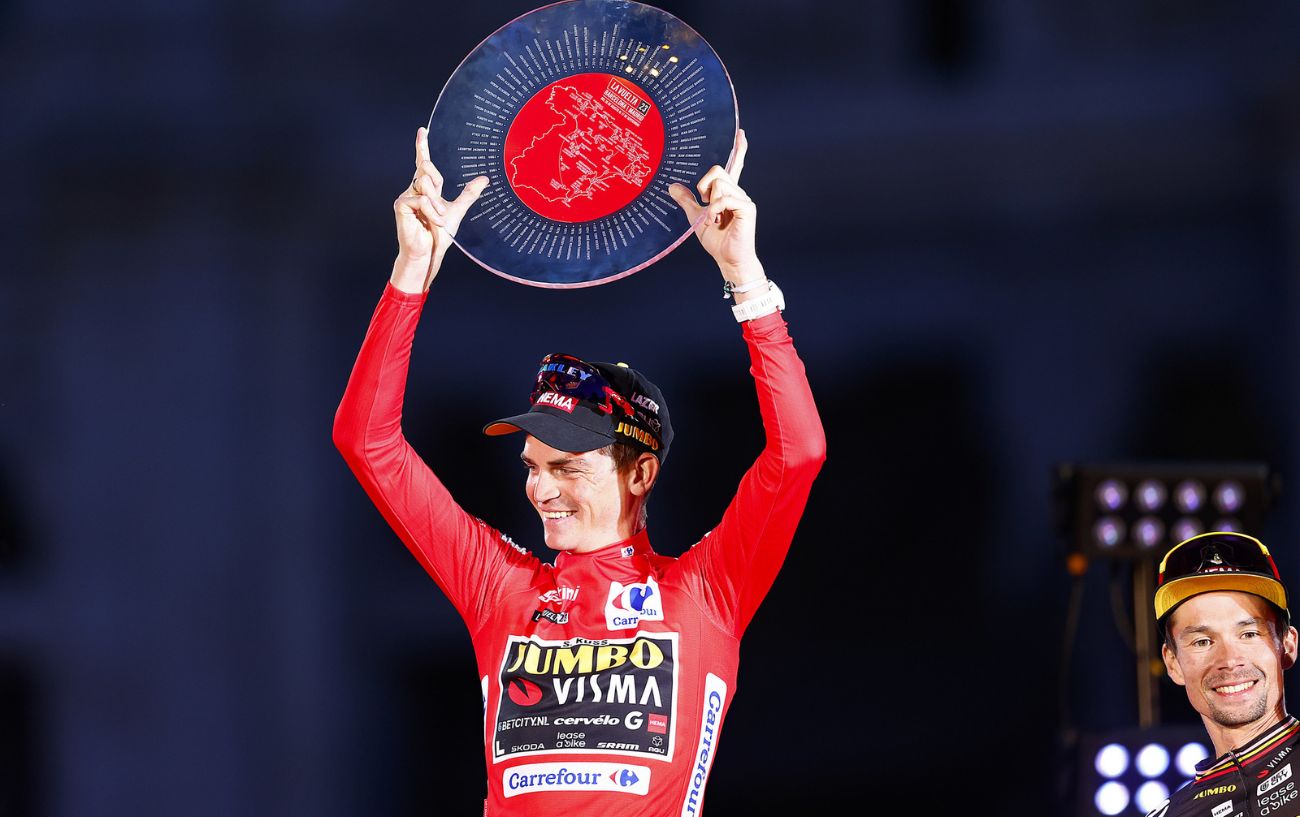 Sepp Kuss raises the trophy for the 2023 Vuelta a Espana above his head on the podium.