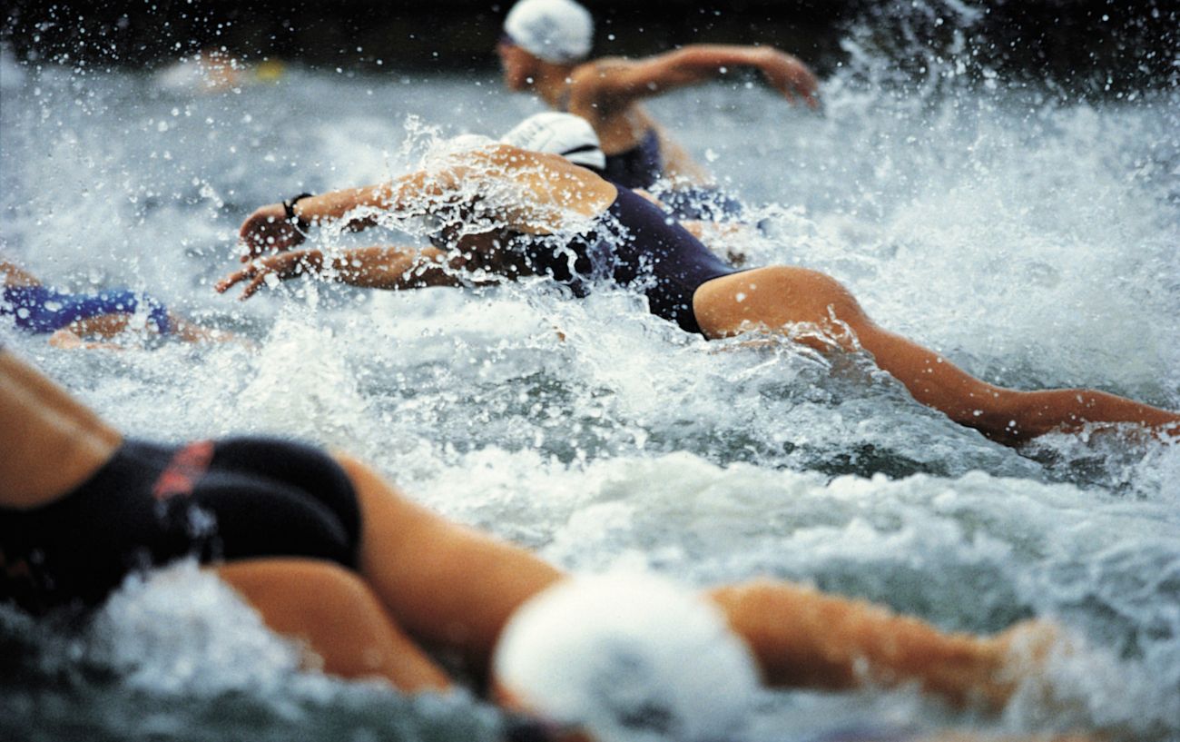A group of triathletes dive into the ocean during an Ironman triathlon distance.