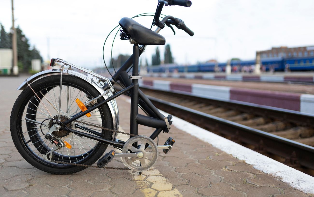 A black folding bike rests on a train station platform.