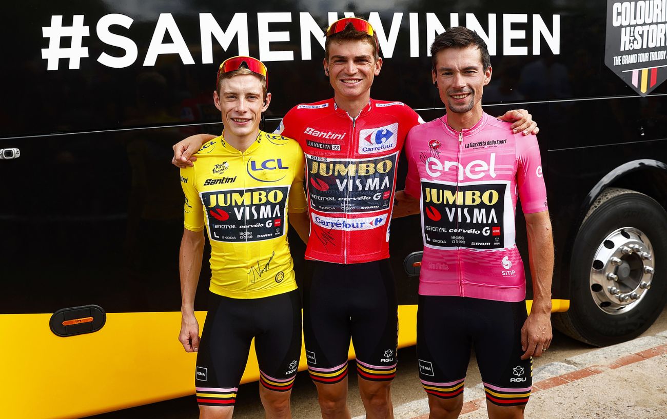 Sepp Kuss, Primoz Roglic, and Jonas Vingegaard pose in their winner's jerseys from the 2023 Vuelta a Espana, Giro d'Italia, and Tour de France respectively.
