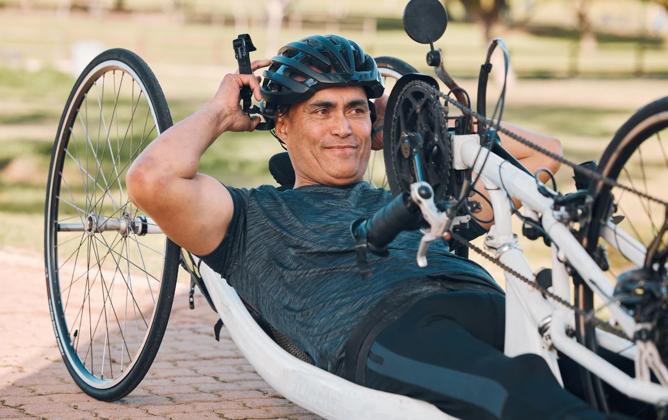 A man wearing a black helmet lies down on a recumbent bicycle.