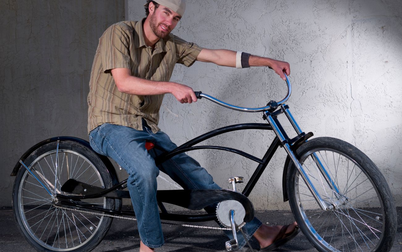 A man wearing a shirt and jeans sits on a black stretch cruiser bike.