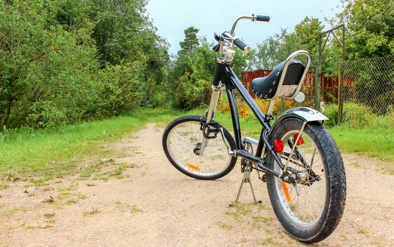 A black chopper style cruiser bike on a gravel path with bushes behind it.