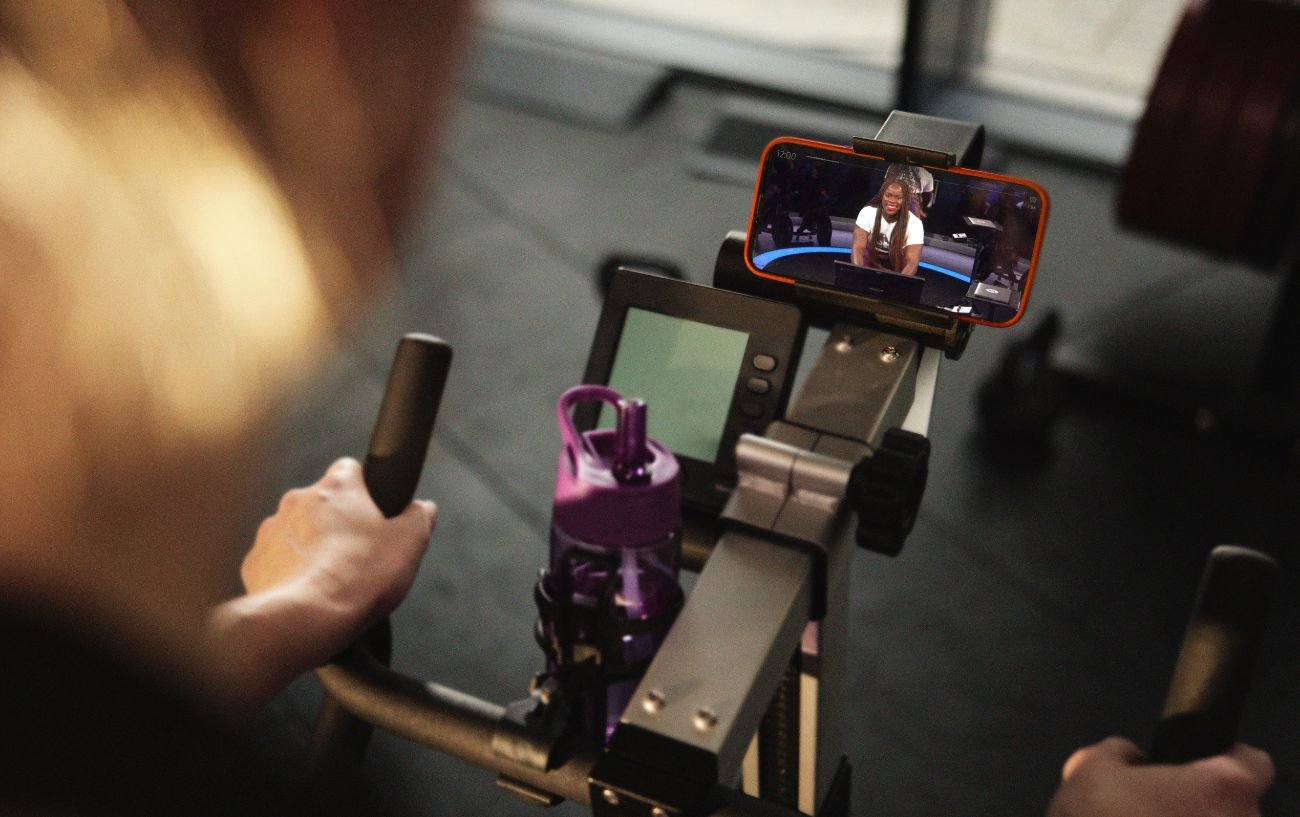 A cyclist uses Peloton without a subscription, following the class on a regular exercise bike.