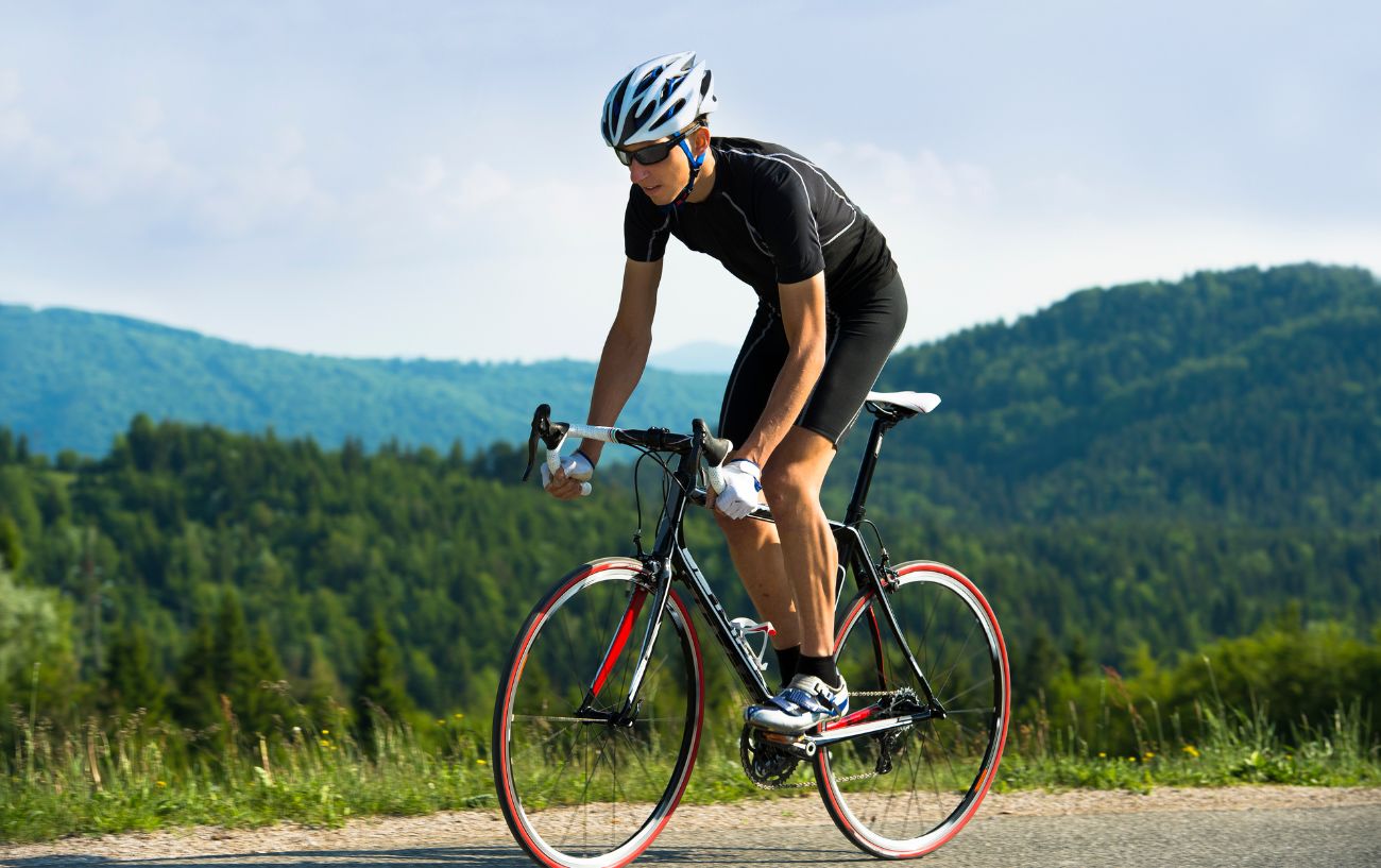 A road cyclist dressed in black climbs in a forested valley.