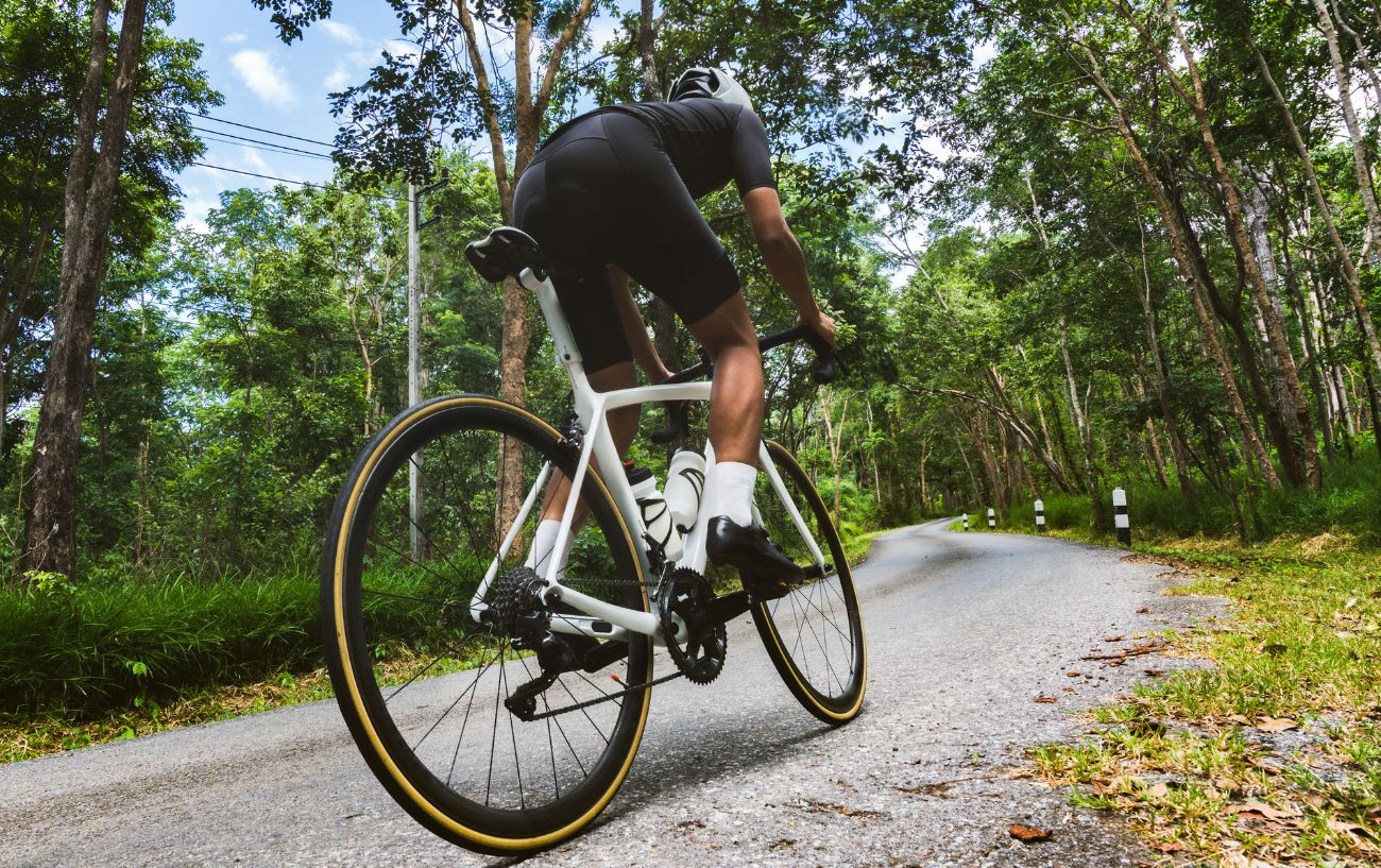 A cyclist on a white road bike climbs a steep hill at a high cycling cadence.