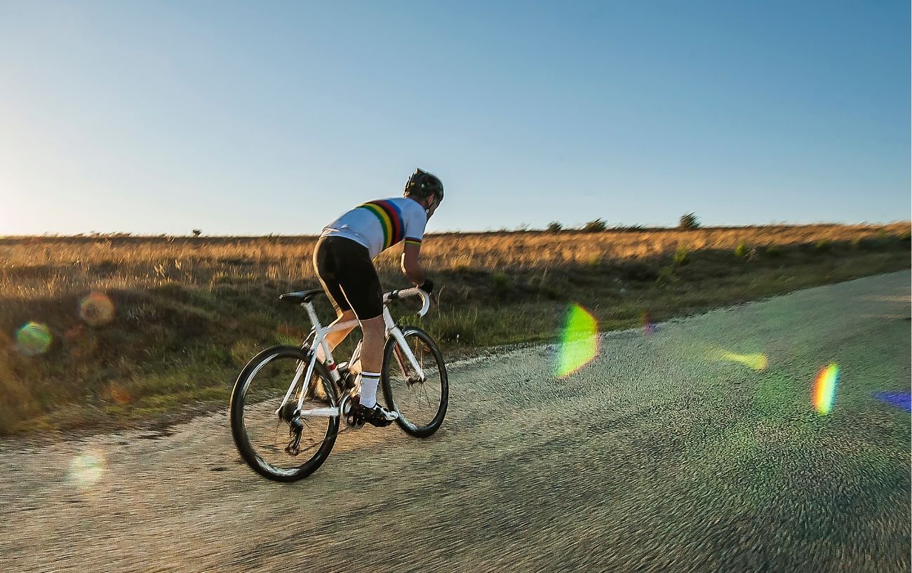 An amateur cyclist attempt to train their cycling cadence while riding a white bike on a gravel road at sunset.