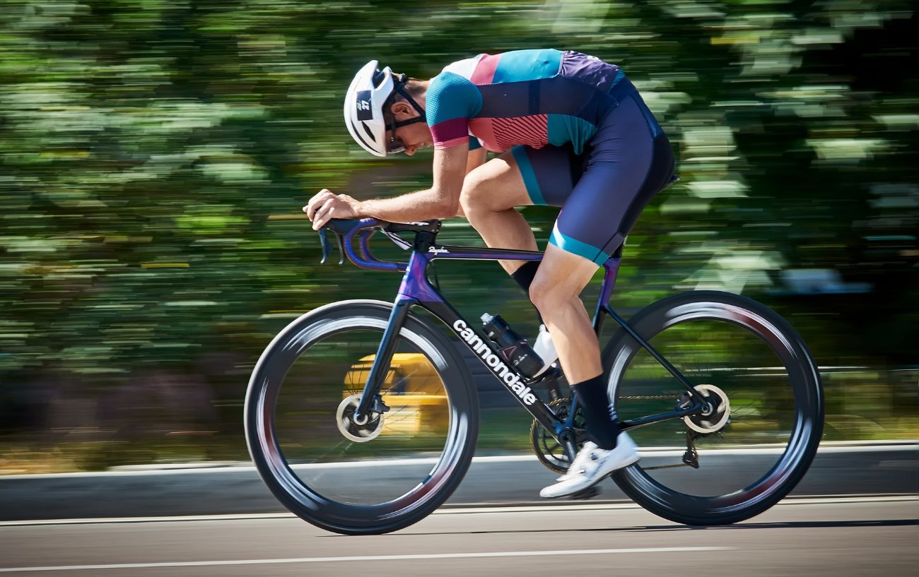 A cyclist rides a purple Cannondale road bike at high speed during a race.
