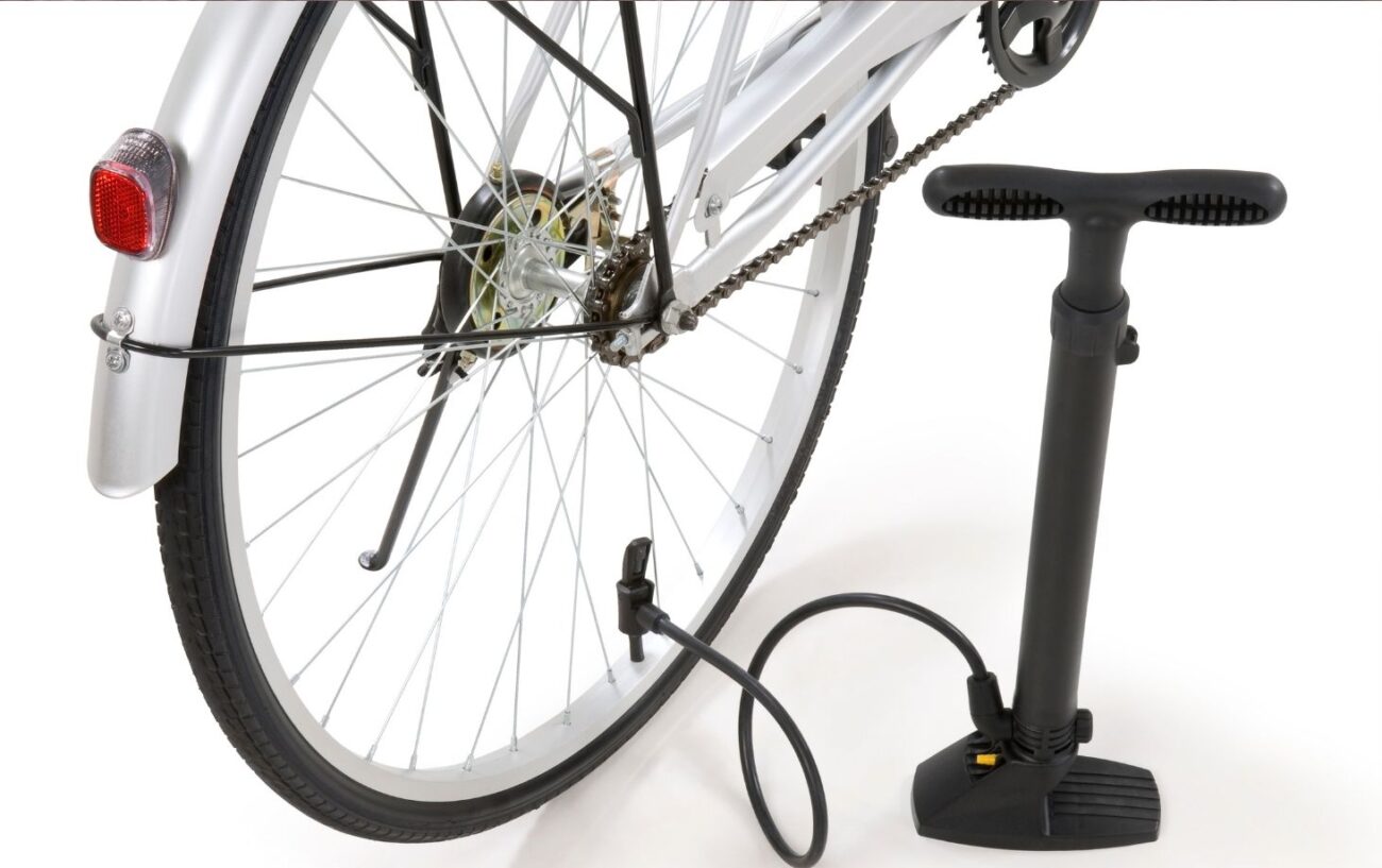 A track pump is connected to the rear wheel of a white hybrid bike.