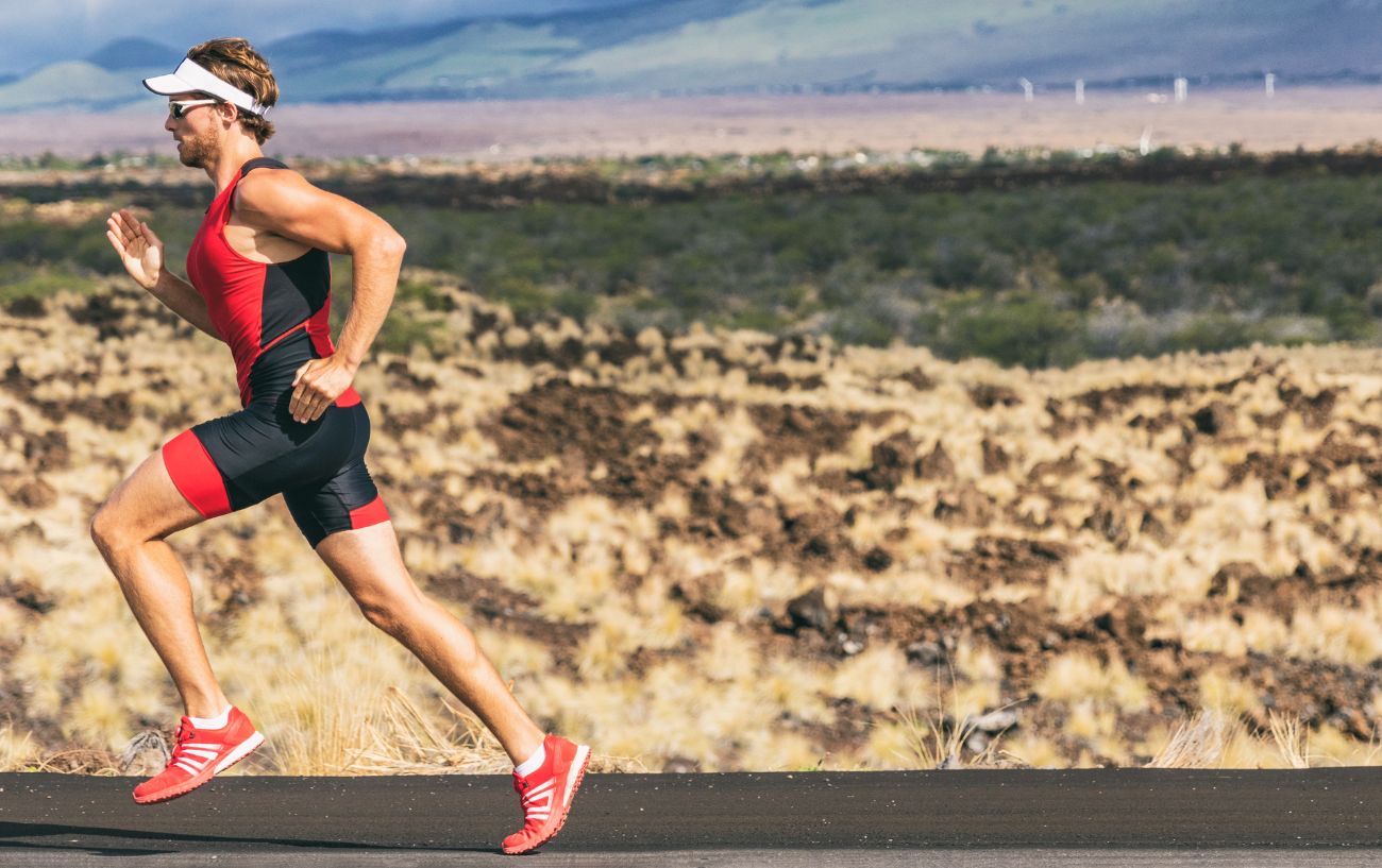 A triathlete wearing red runs along a tarmac road.