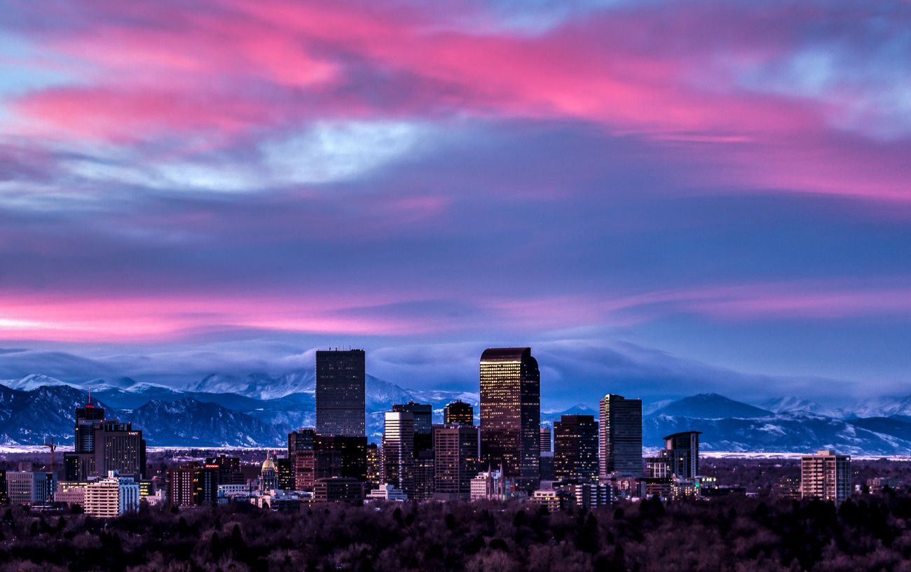 Denver's skyline at sunset, with the Rocky Mountains behind.