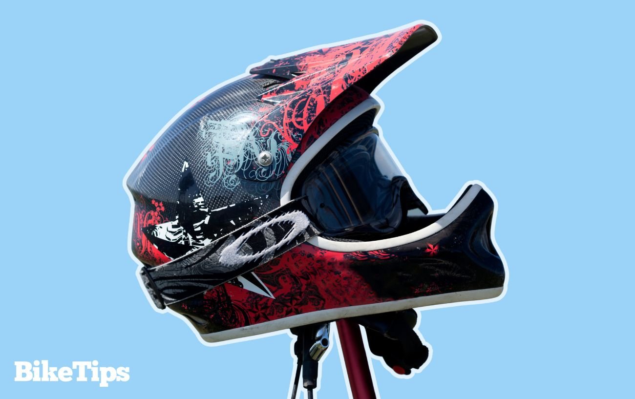 A full-face mountain bike helmet with Oakley goggles attached on a blue background.